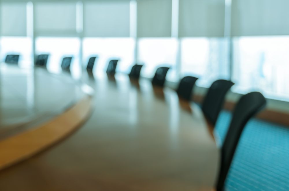 Blurred conference room with a curved table and black chairs by a bright window