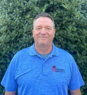Man in a blue polo shirt standing outdoors in front of green bushes