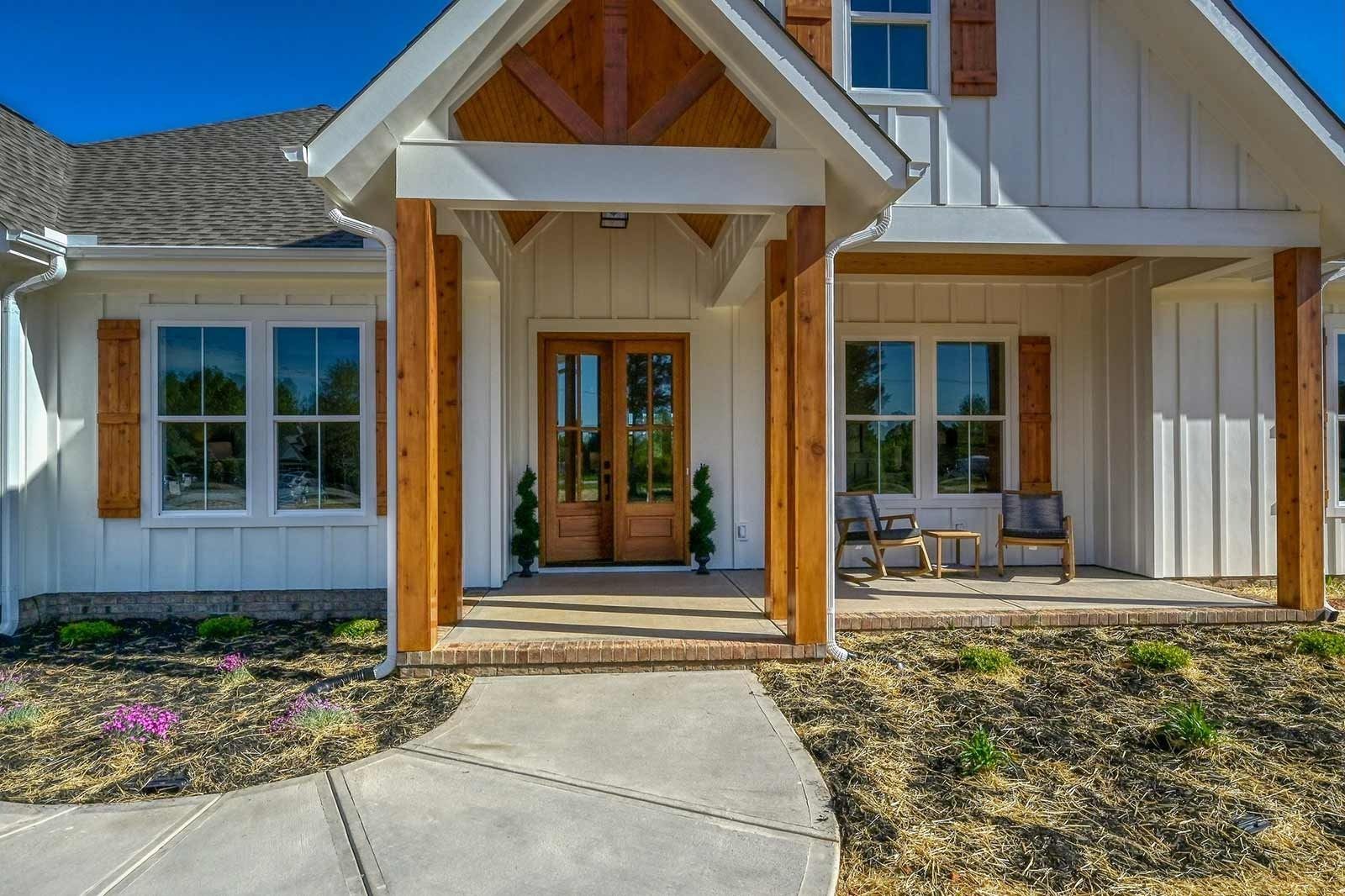 Front entrance of a modern house with white siding, wooden posts, and a curved walkway.