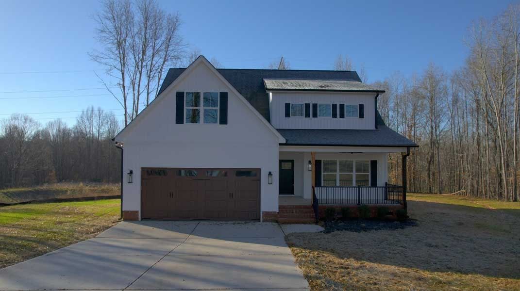 White two-story house with attached garage, front porch, and long driveway on a sunny day
