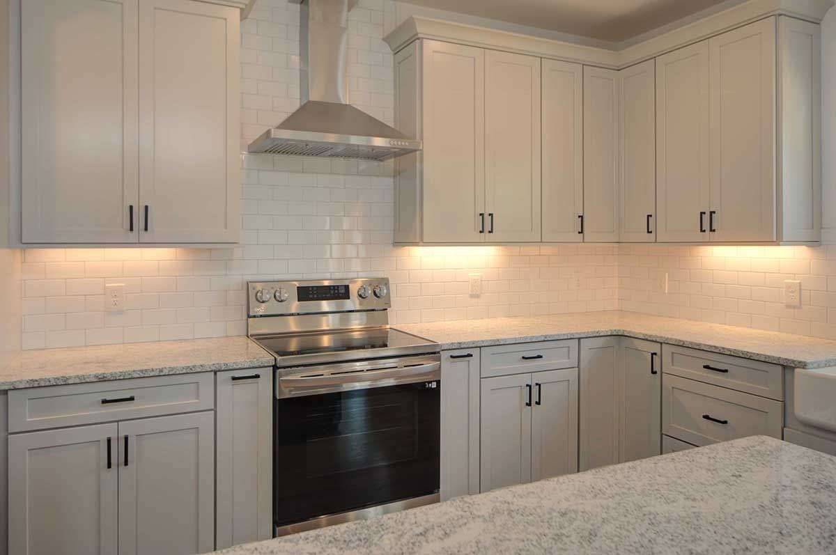 Bright white kitchen with gray cabinets, stainless steel appliances, subway tile backsplash, and granite island countertop
