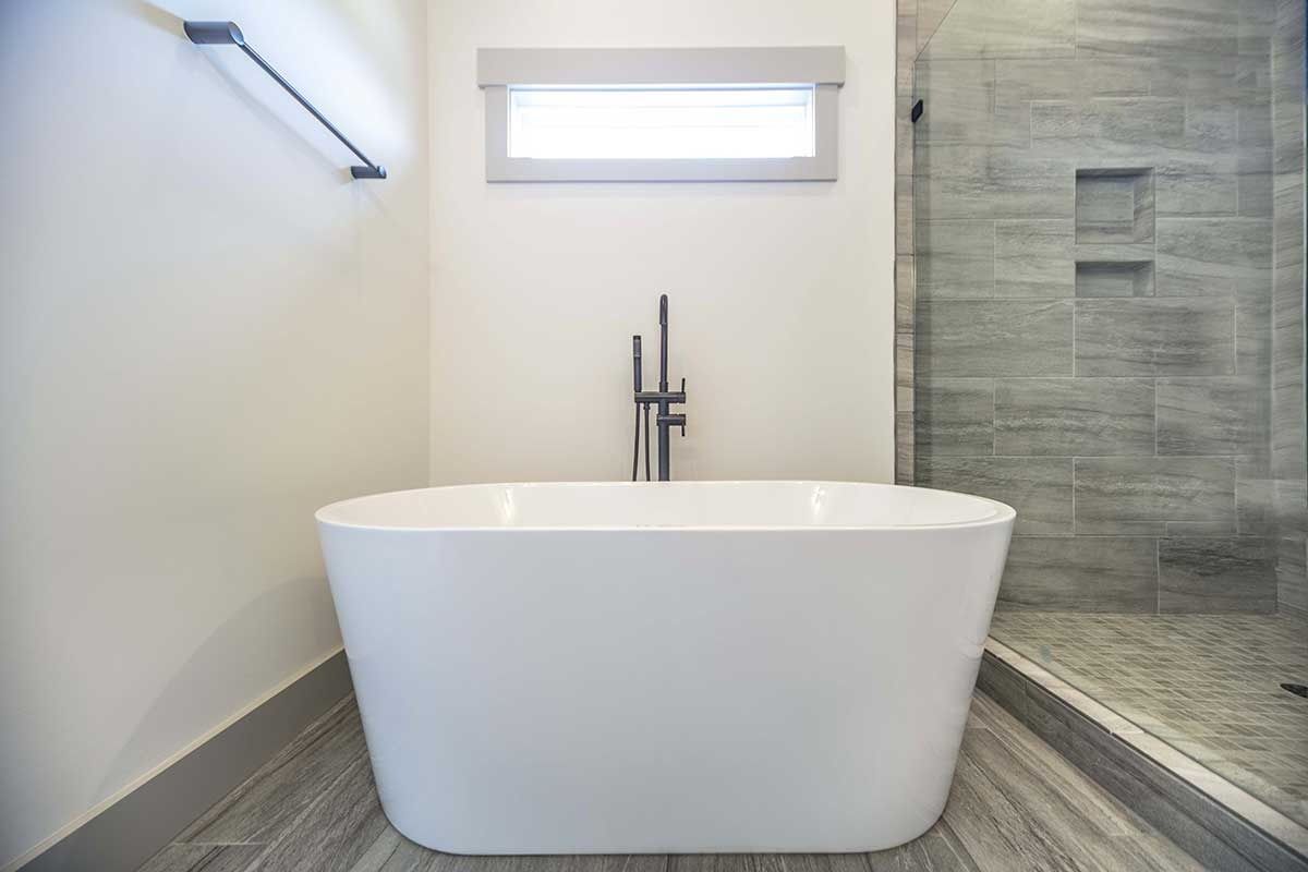 Modern bathroom with a freestanding white tub, gray tile shower, and small window