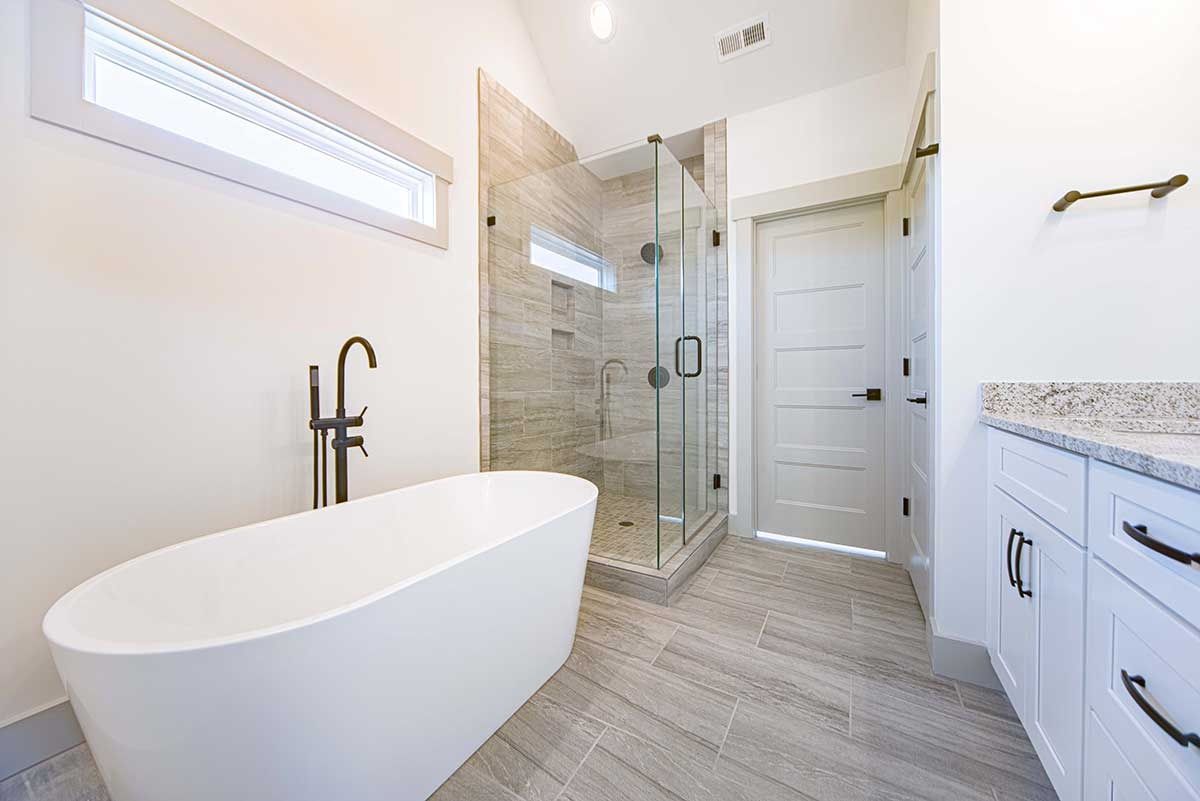 Bright modern bathroom with freestanding tub, glass shower, white vanity, and tiled floor