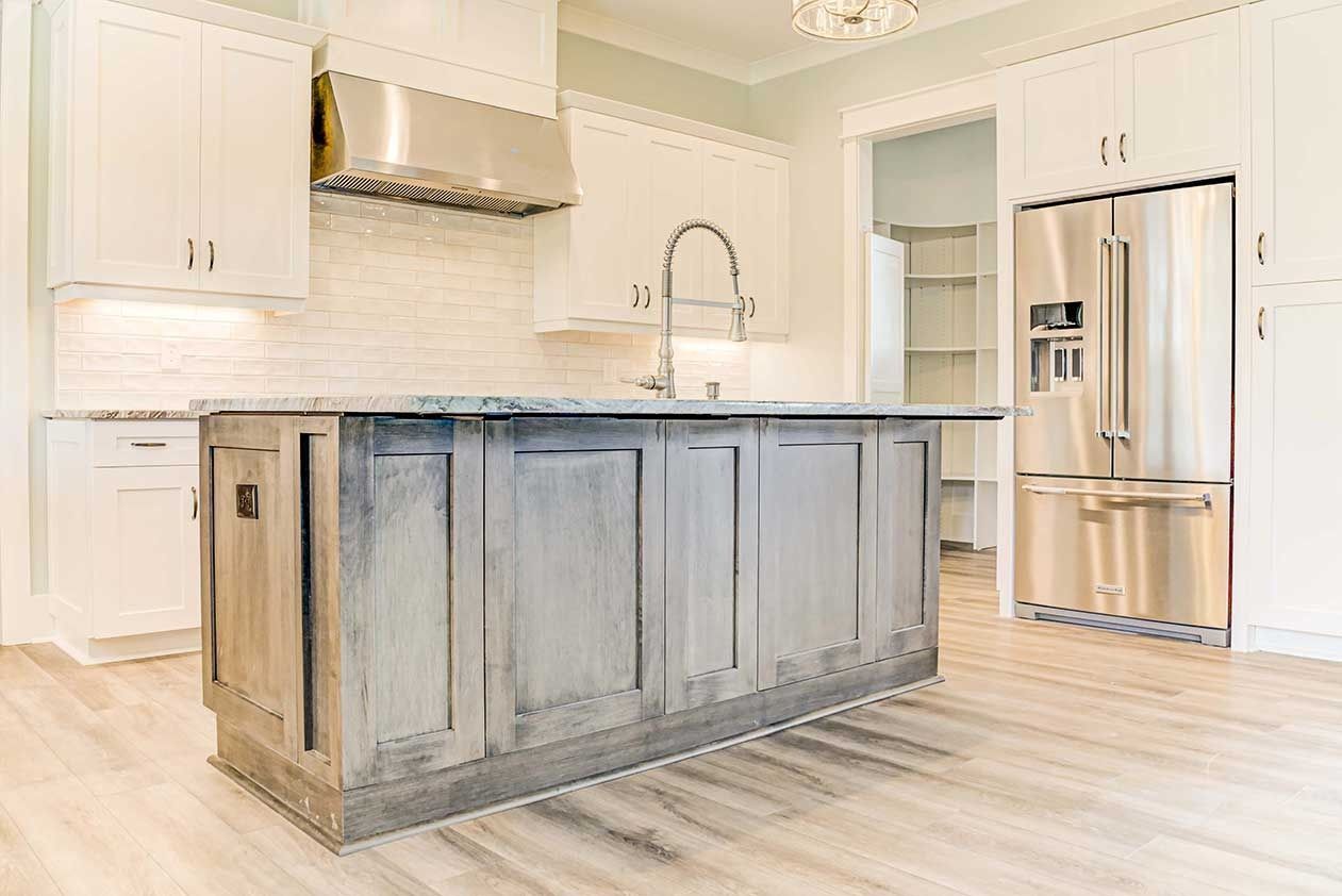 Modern white kitchen with rustic gray island, stainless fridge, and light wood floors