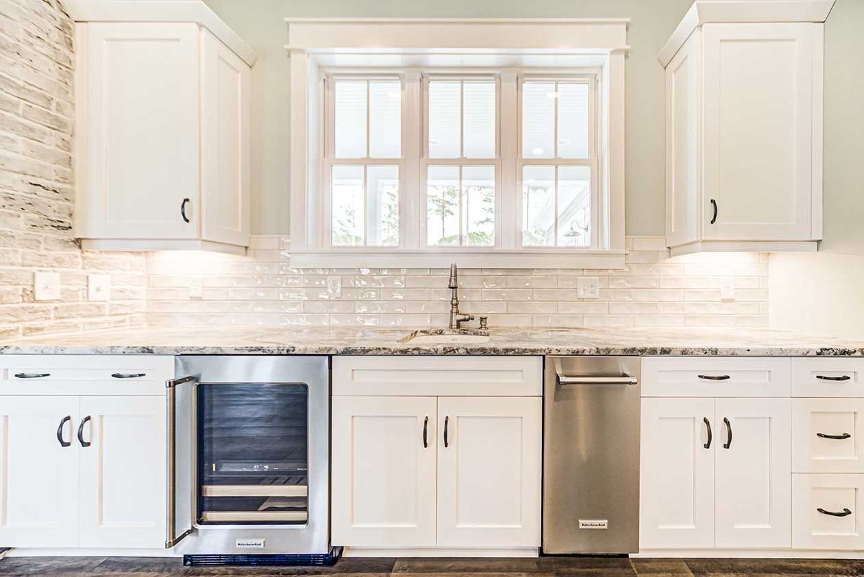 Bright white kitchen with cabinets, window over sink, marble backsplash, and stainless steel dishwasher and oven.