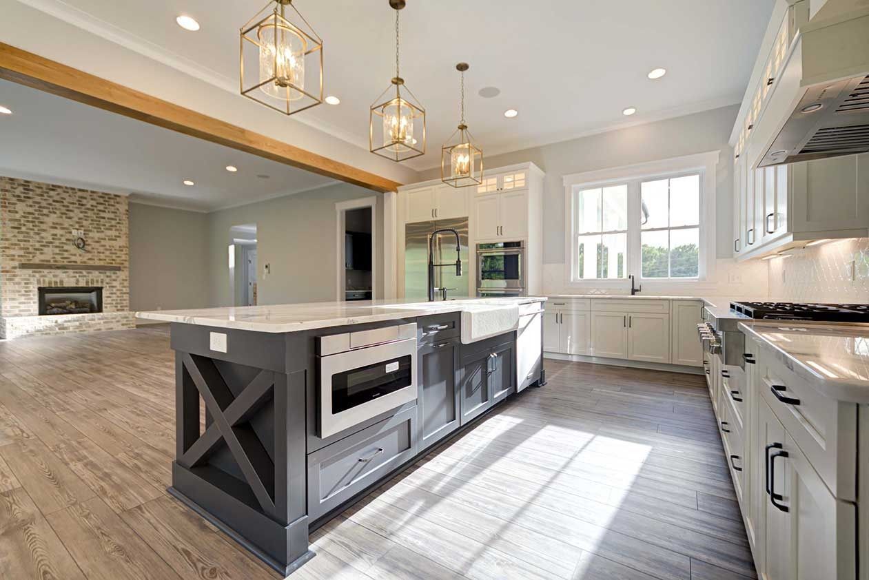Bright modern kitchen with large island, white cabinets, pendant lights, and stone fireplace visible in the background.