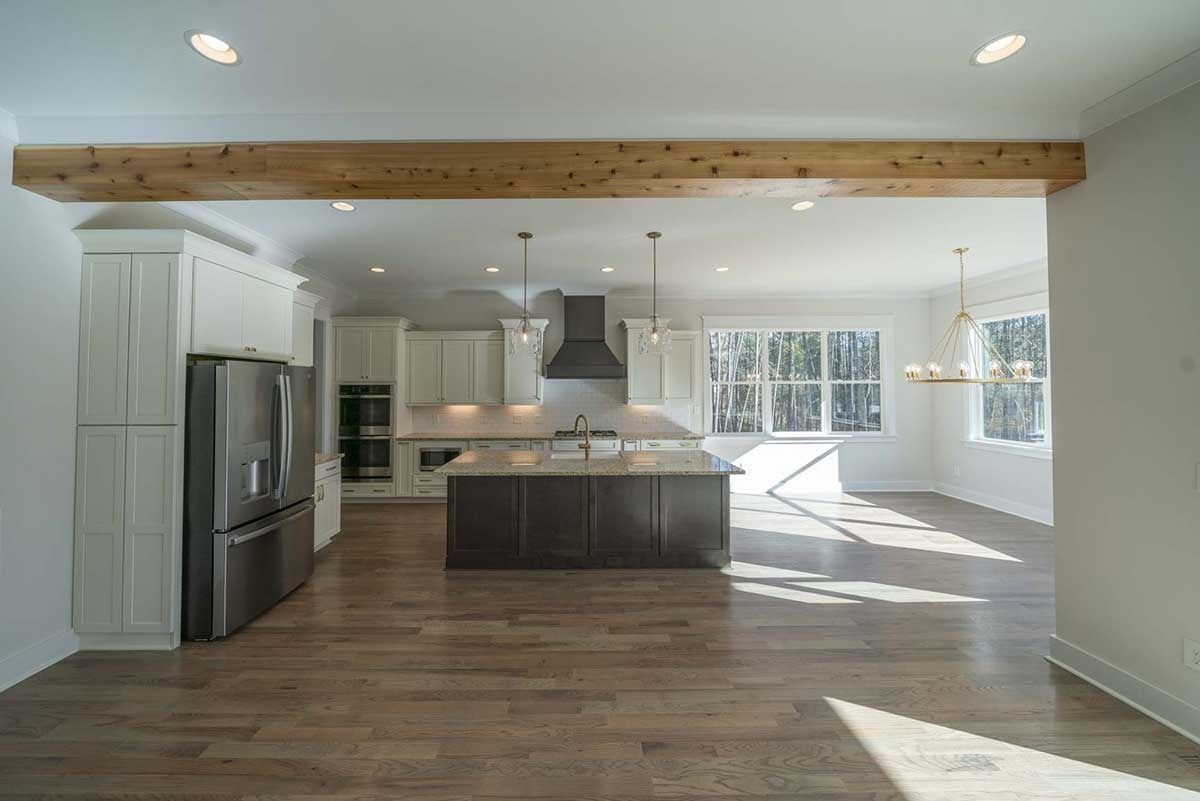 Bright open-plan kitchen and living area with wood floors, white walls, and large windows.