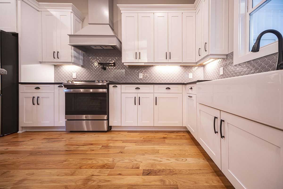 Bright white kitchen with stainless steel appliances, wood floors, and black countertops