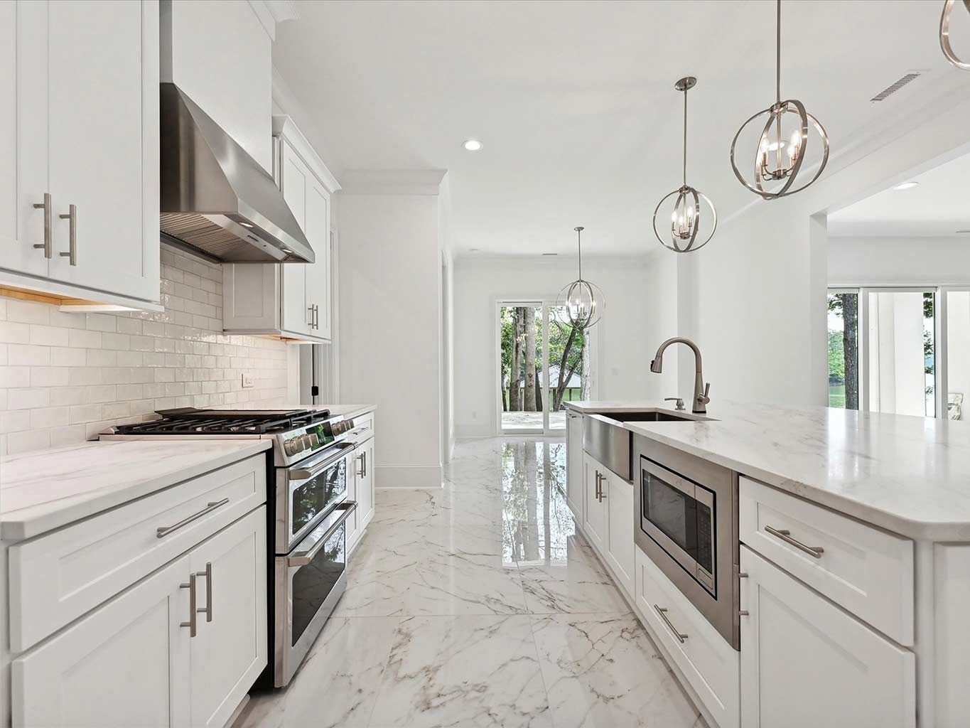 Bright white modern kitchen with marble countertops, stainless appliances, and pendant lights