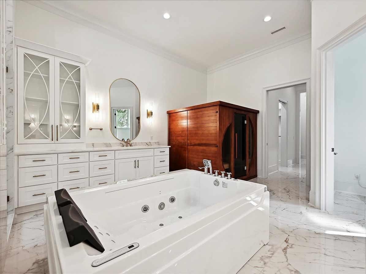 Bright white bathroom with a large soaking tub, double vanity, glass shower, and wooden armoire