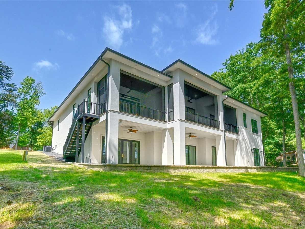 Modern two-story white and gray house with large windows, surrounded by trees and green lawn.