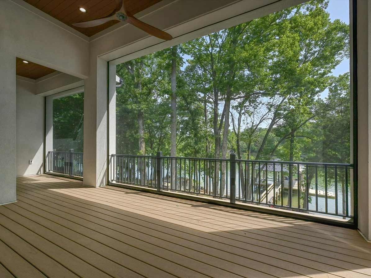 Covered wooden deck with black railing overlooking trees and water