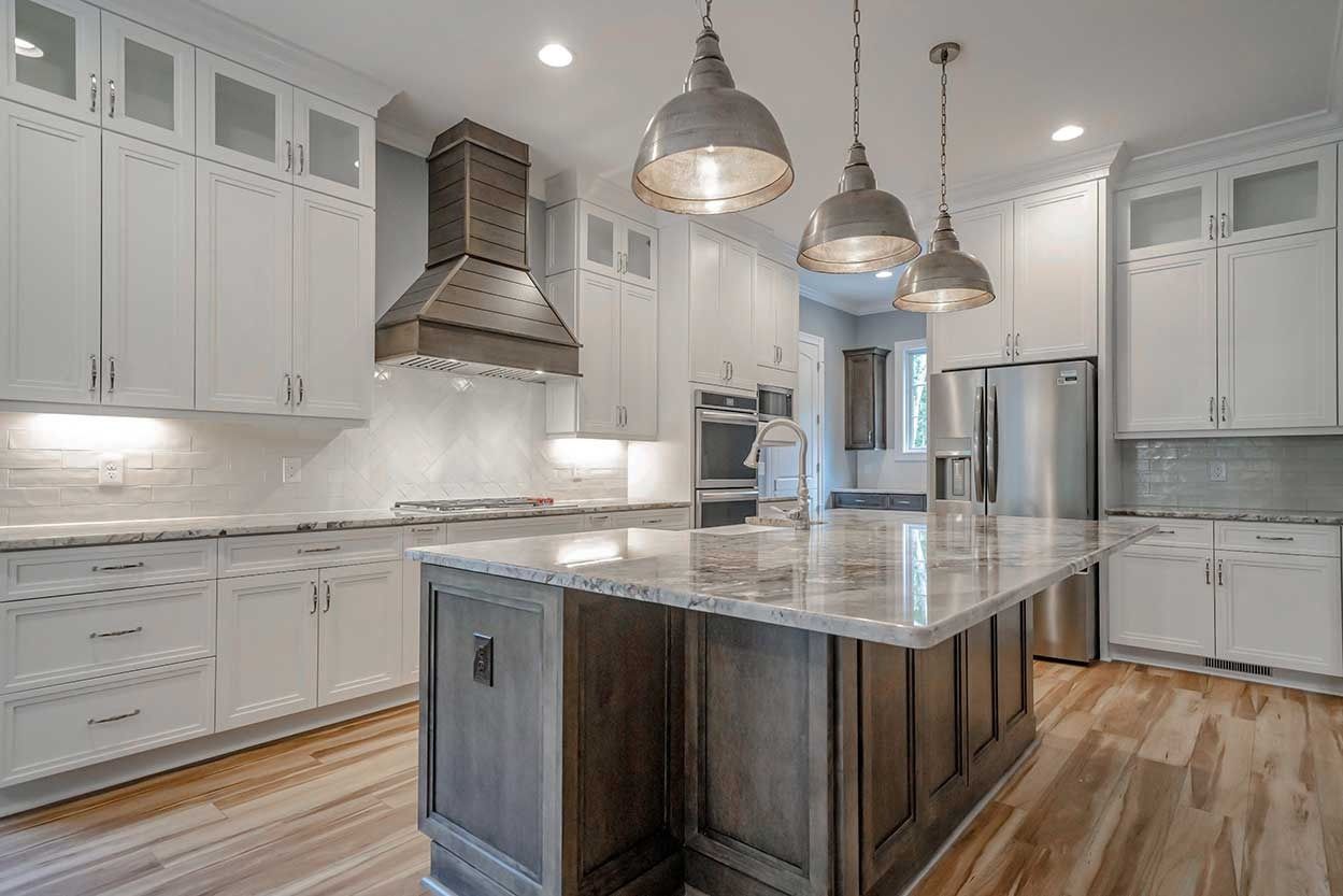 Modern kitchen with white cabinets, marble island, stainless range hood, and pendant lights