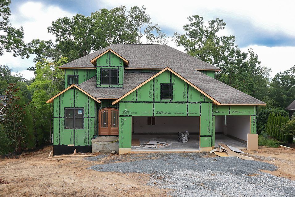 Green house under construction with unfinished siding, front porch, and garage on a gravel lot