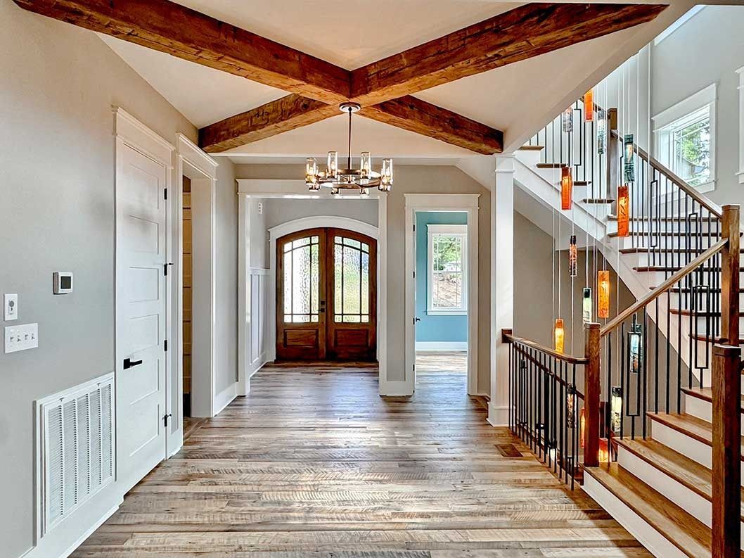 Bright entry hall with wood floors, exposed ceiling beams, staircase, and front doors in the distance