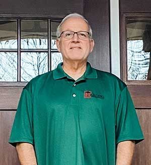 Man standing in front of a building, wearing a green polo shirt and glasses.