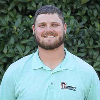 Smiling man in a mint polo shirt standing in front of green foliage