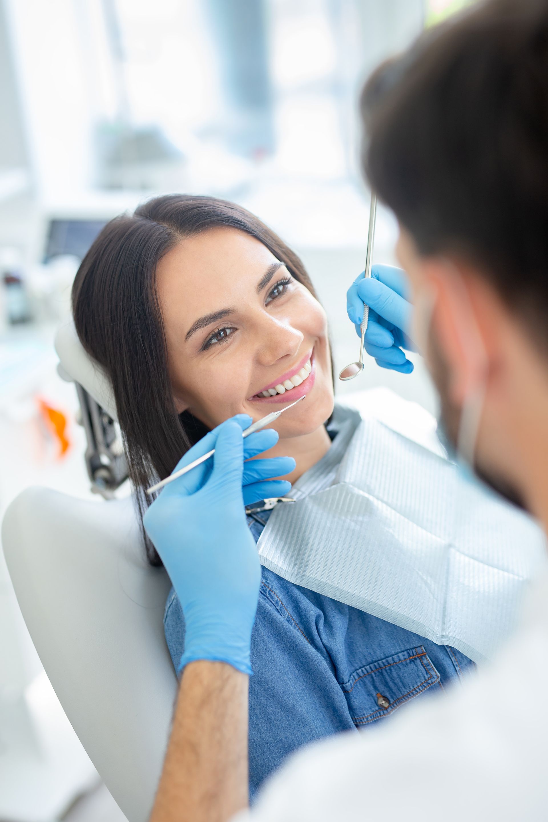 Woman in dental chair smiling, dentist examining her teeth with tools.