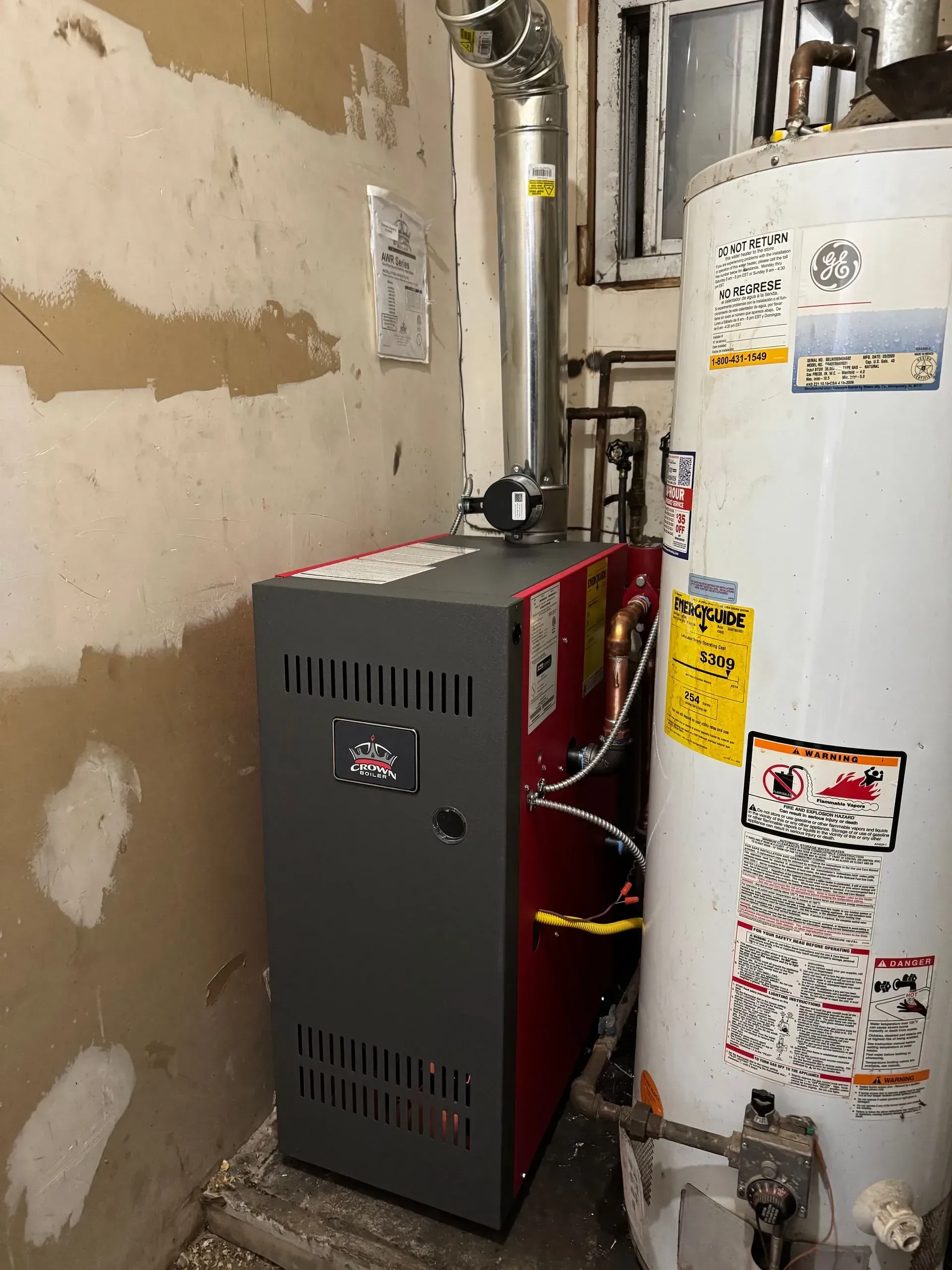 Furnace and water heater in a basement. The furnace is gray and red. The water heater is white.