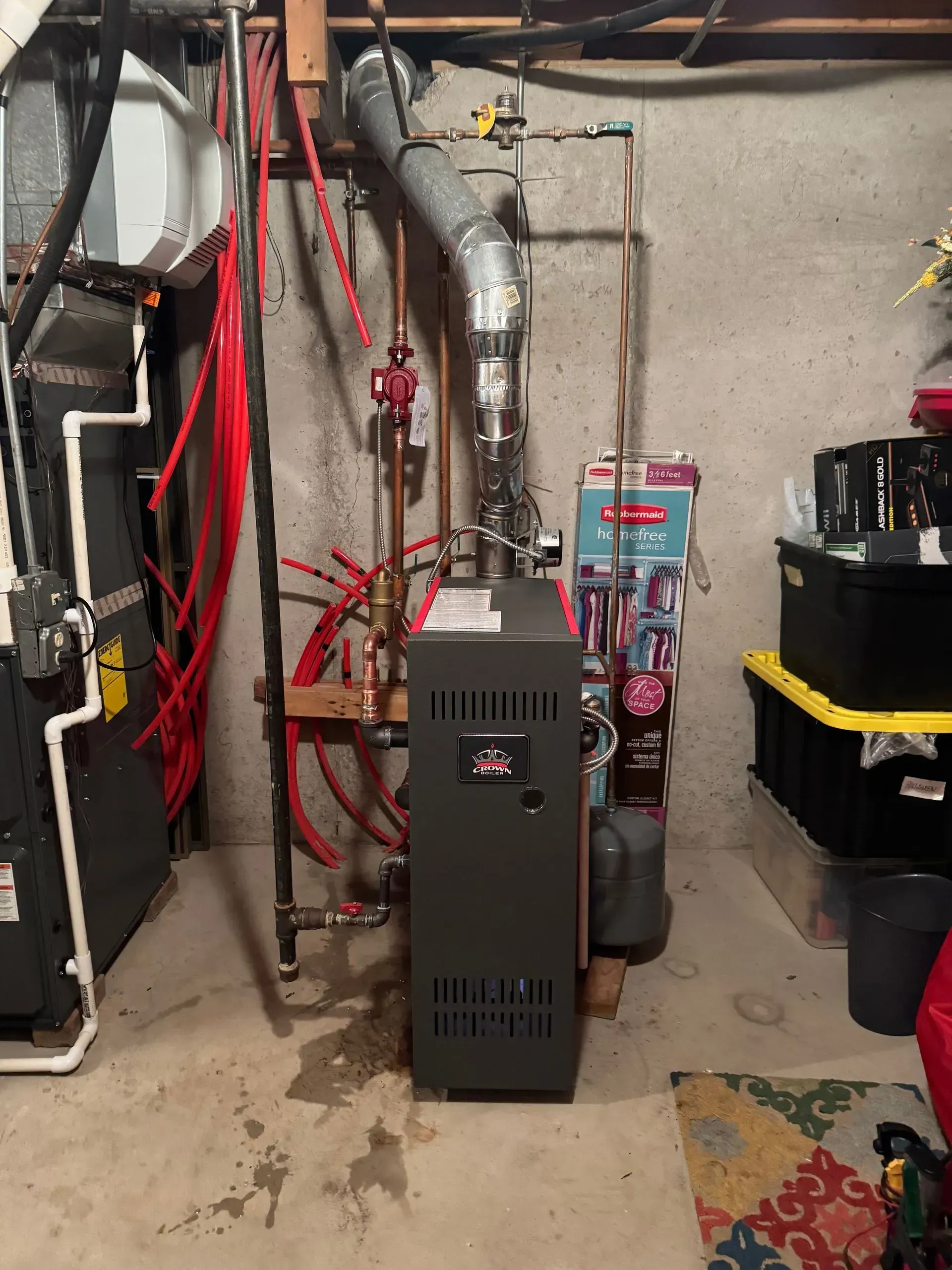 Furnace and associated pipes and equipment in a basement. Concrete floor, gray furnace, red pipes.