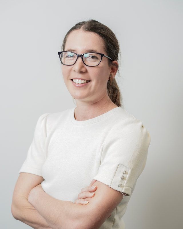 A woman wearing glasses and a white shirt is smiling with her arms crossed.