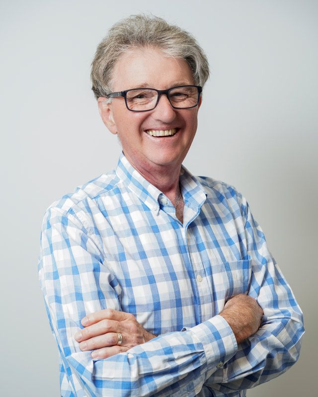 A man wearing glasses and a plaid shirt is smiling with his arms crossed.