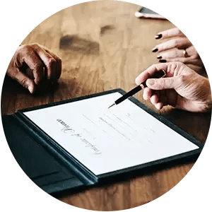 A person is signing a document with a pen on a wooden table.