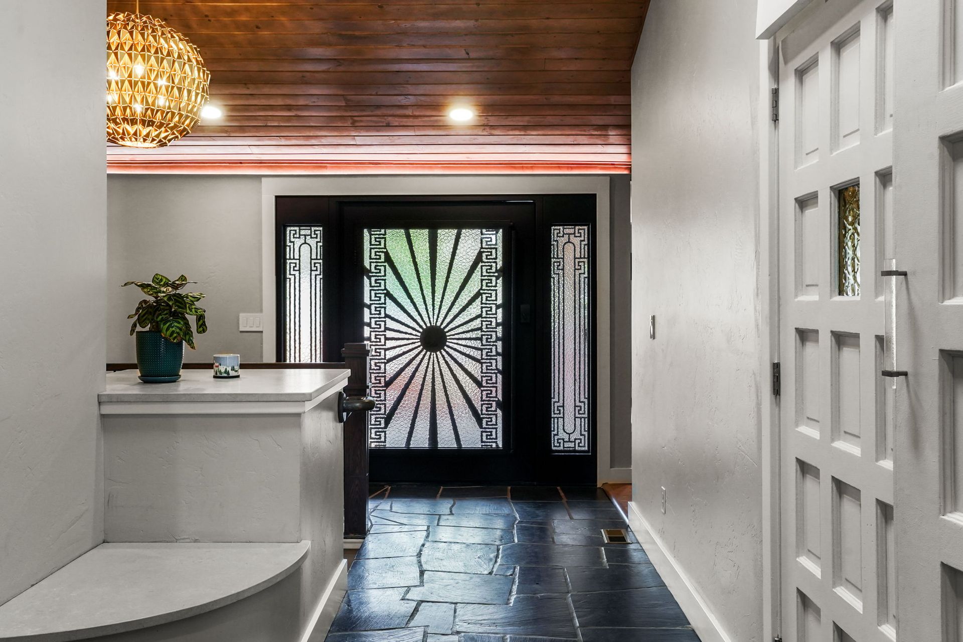 Modern entryway with white walls, wood ceiling, black tiled floor, and decorative front door.