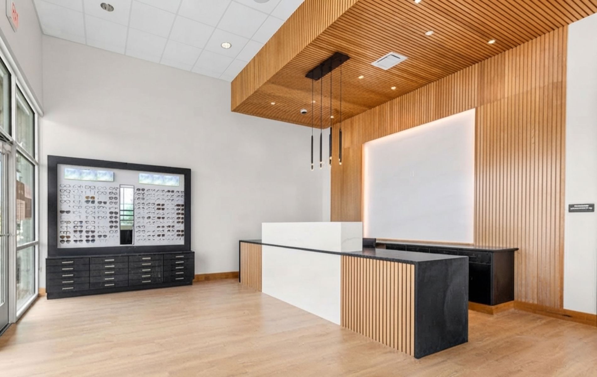 Modern lobby with light wood finishes, white walls, a black front desk, and a mounted board display