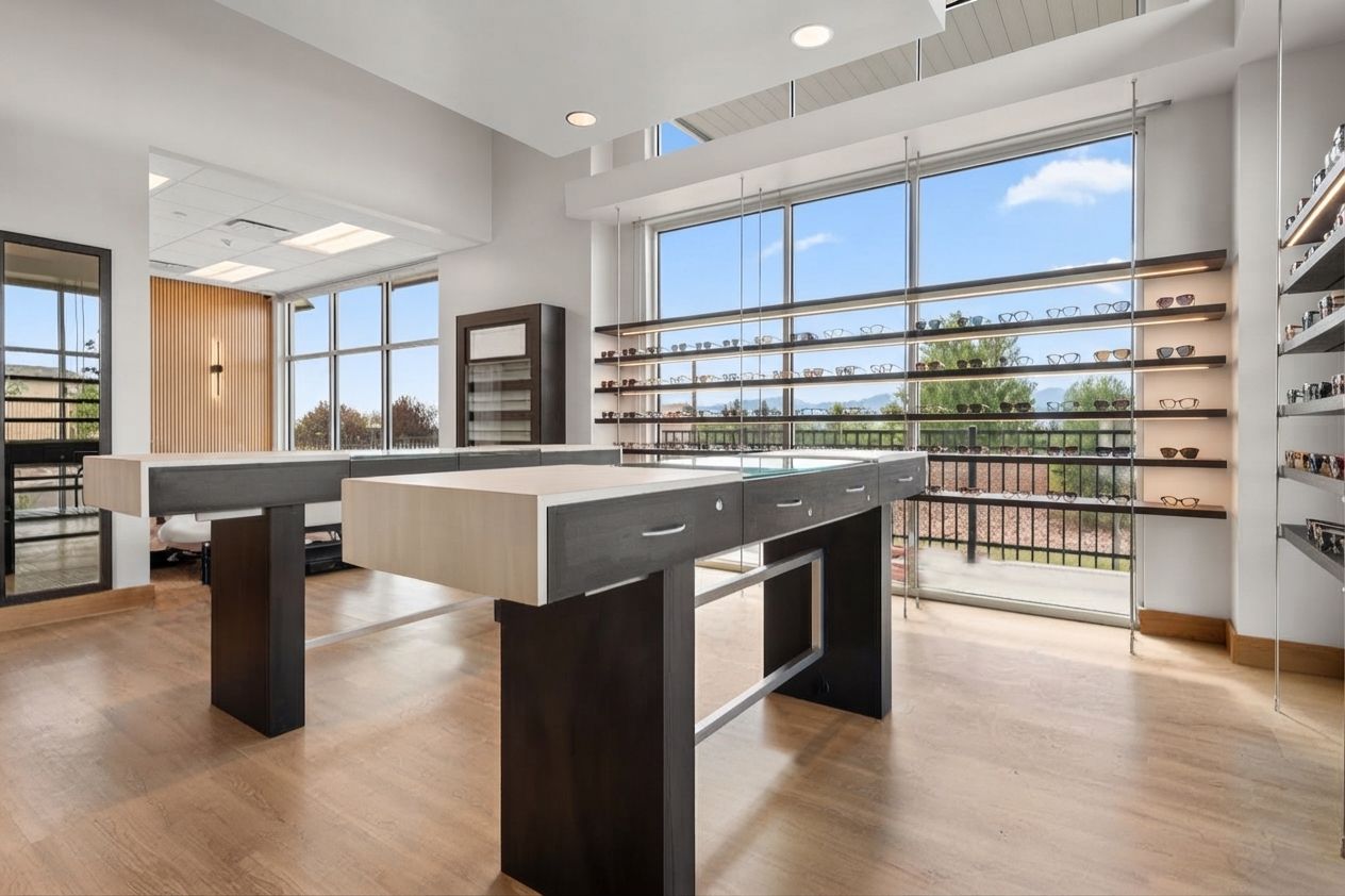 Bright modern boutique with white counters, wood floors, and wall-mounted shelves by large windows.