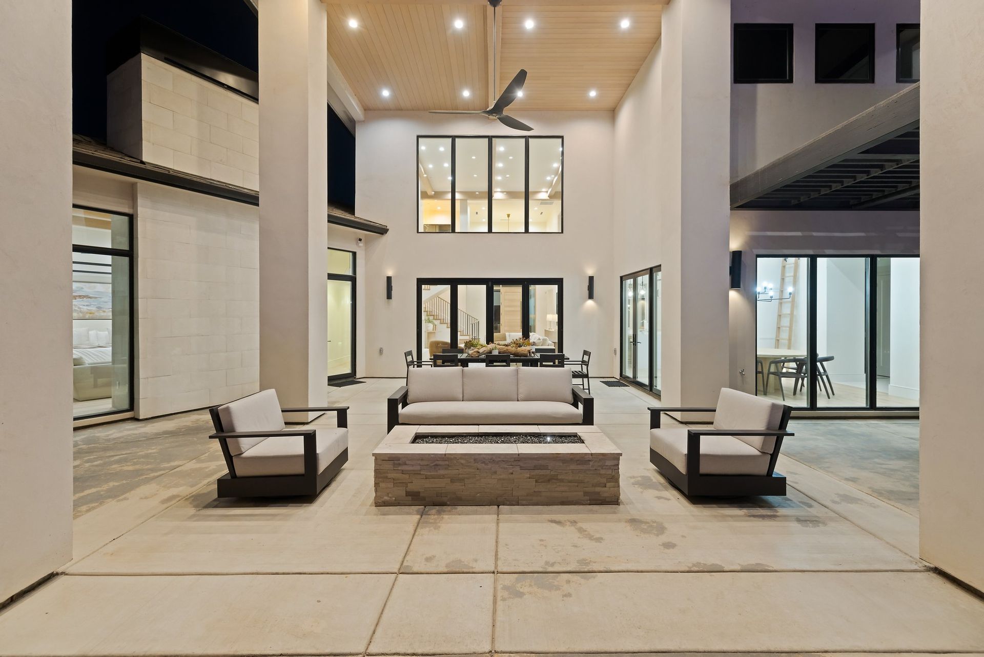 Modern open-air patio with white sofas, armchairs, and a central coffee table under recessed ceiling lights.