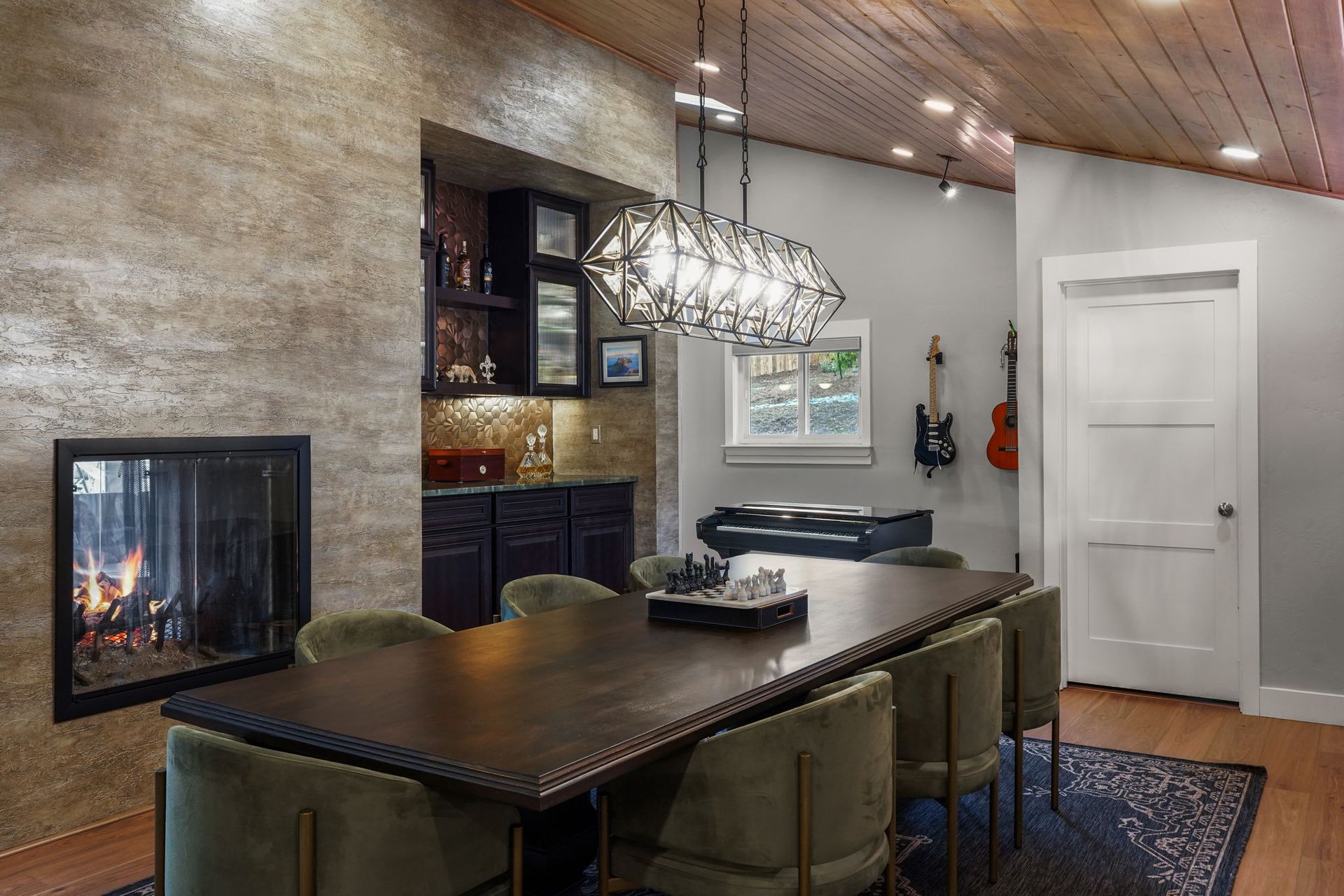Modern basement bar with fireplace, pool table, pendant lights, and wall-mounted guitars
