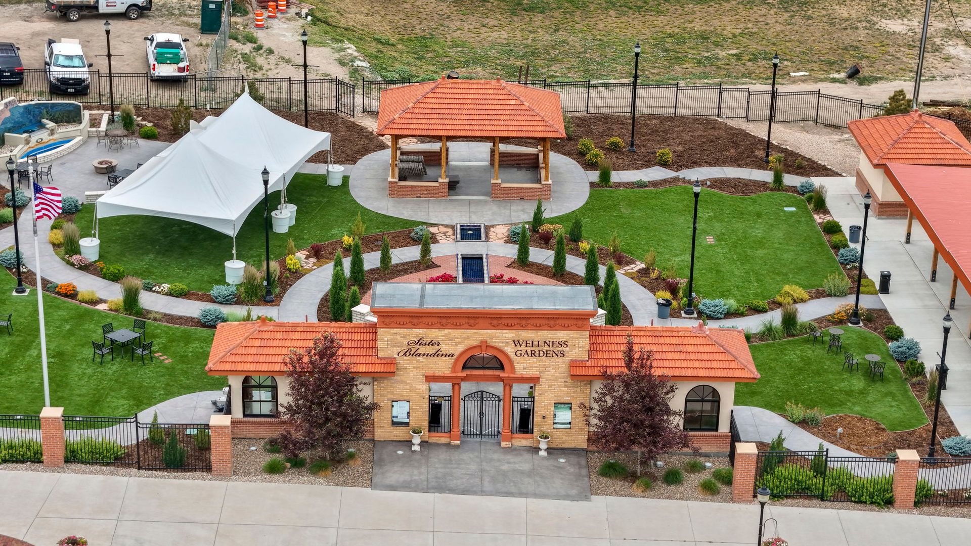 Aerial view of a small park with a central stone arch entrance, red tile roofs, pathways, and greenery.
