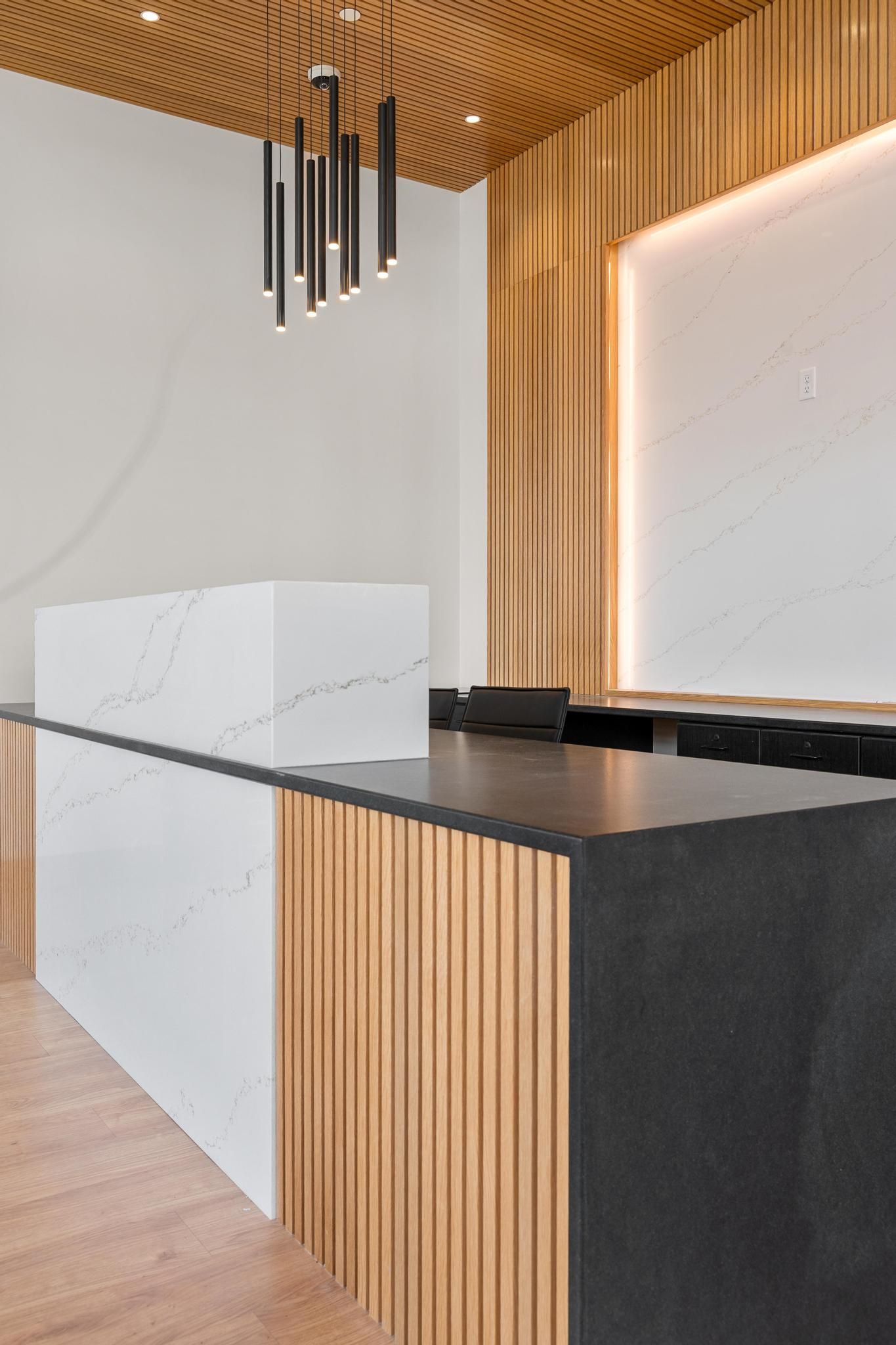 Modern reception desk with wood slat walls, black stone counter, and white cabinetry in a minimalist lobby