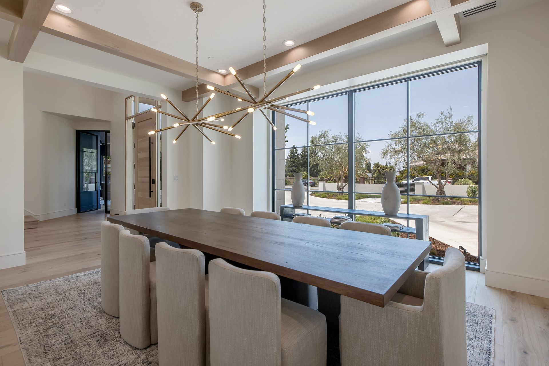 Modern dining room with a long table, beige chairs, and large windows overlooking a bright patio