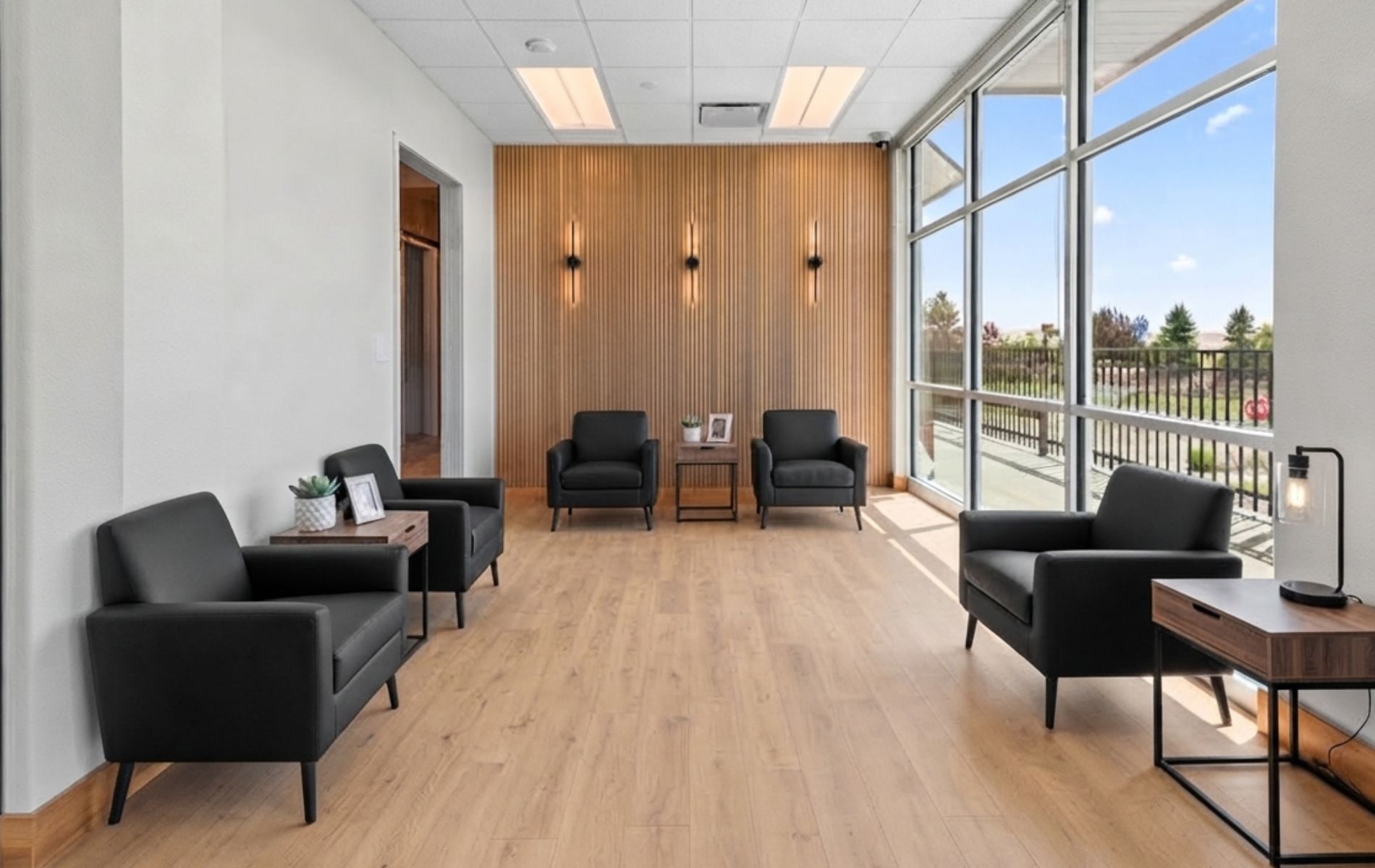 Modern waiting room with black chairs, light wood floor, and large windows.