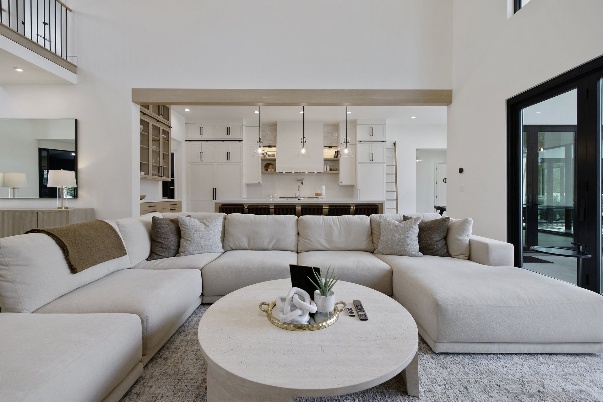 Bright modern living room with a white sectional sofa and round coffee table, open kitchen in the background
