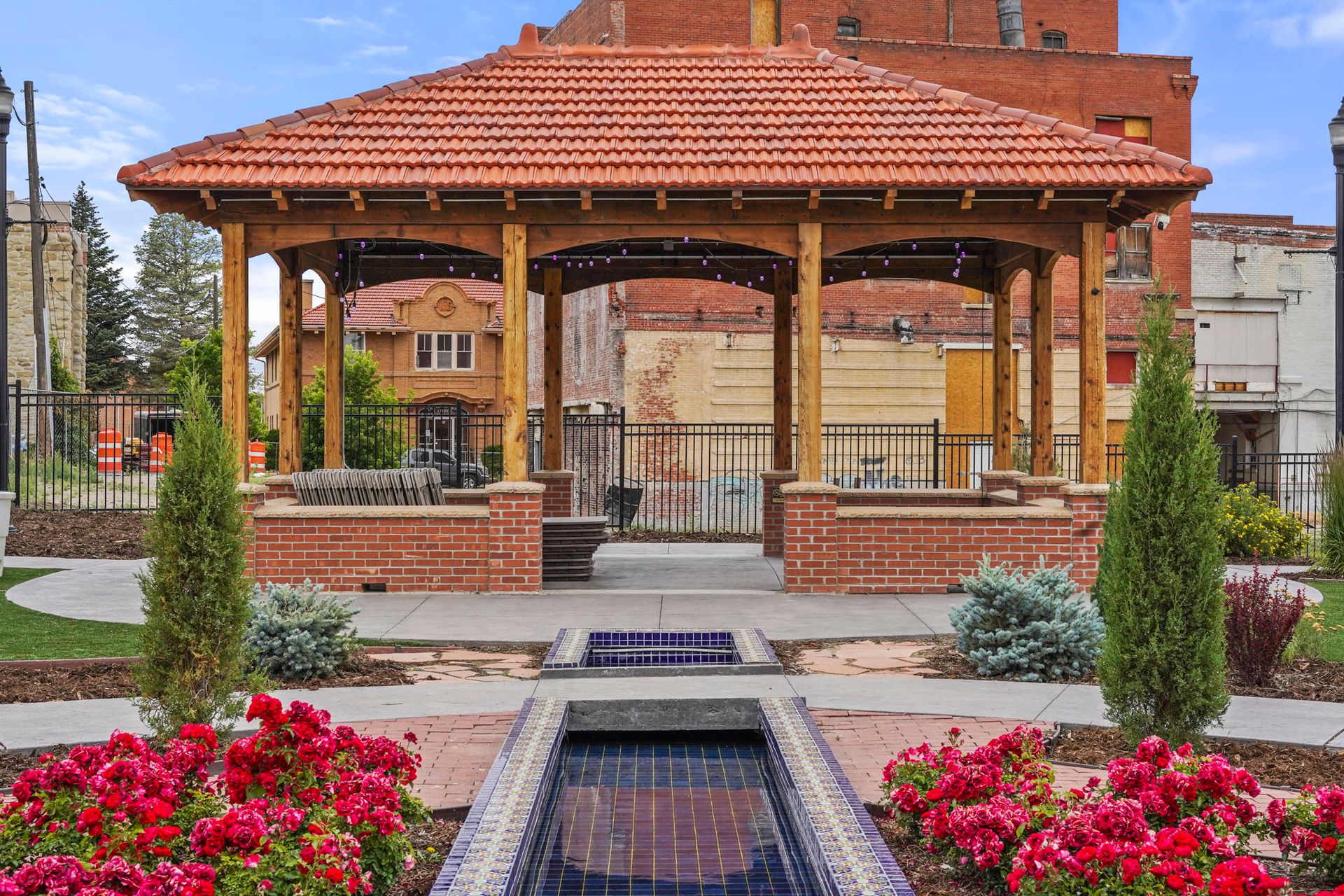 Red brick gazebo in a landscaped plaza with flower beds and a fountain in front