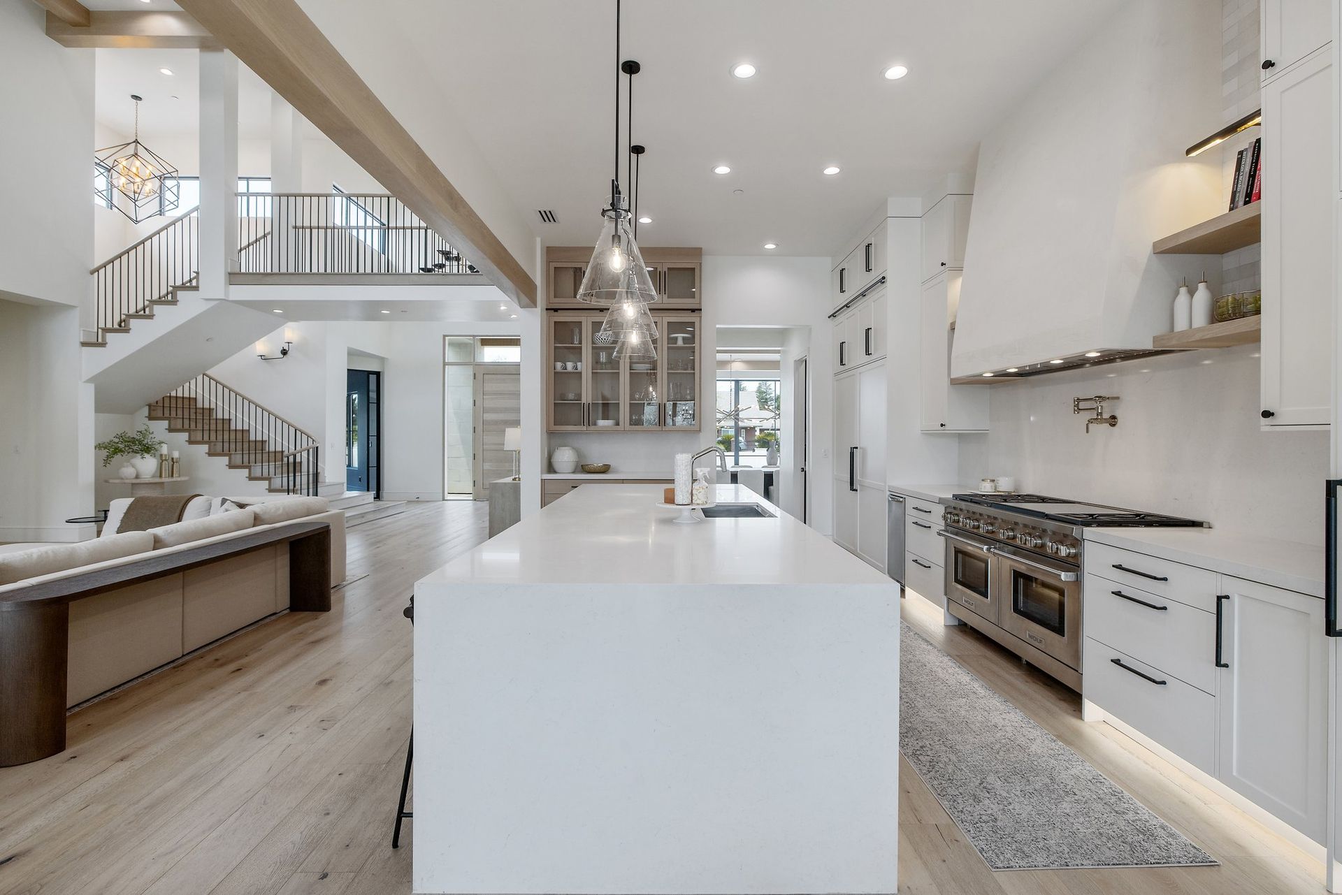 Bright modern white kitchen with island, stainless appliances, staircase, and open shelving