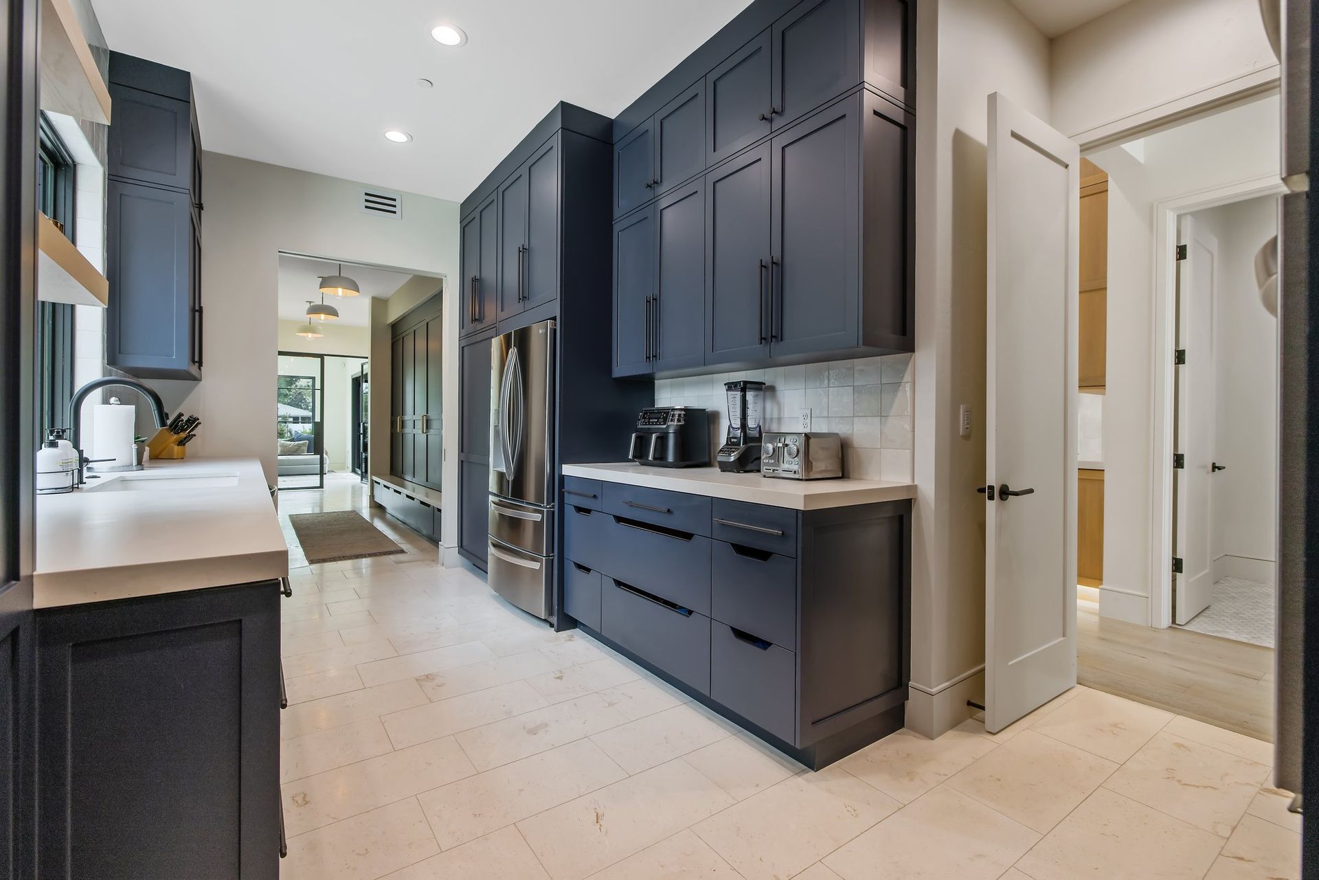 Modern kitchen hallway with dark navy cabinets, light tile floor, and stainless steel appliances