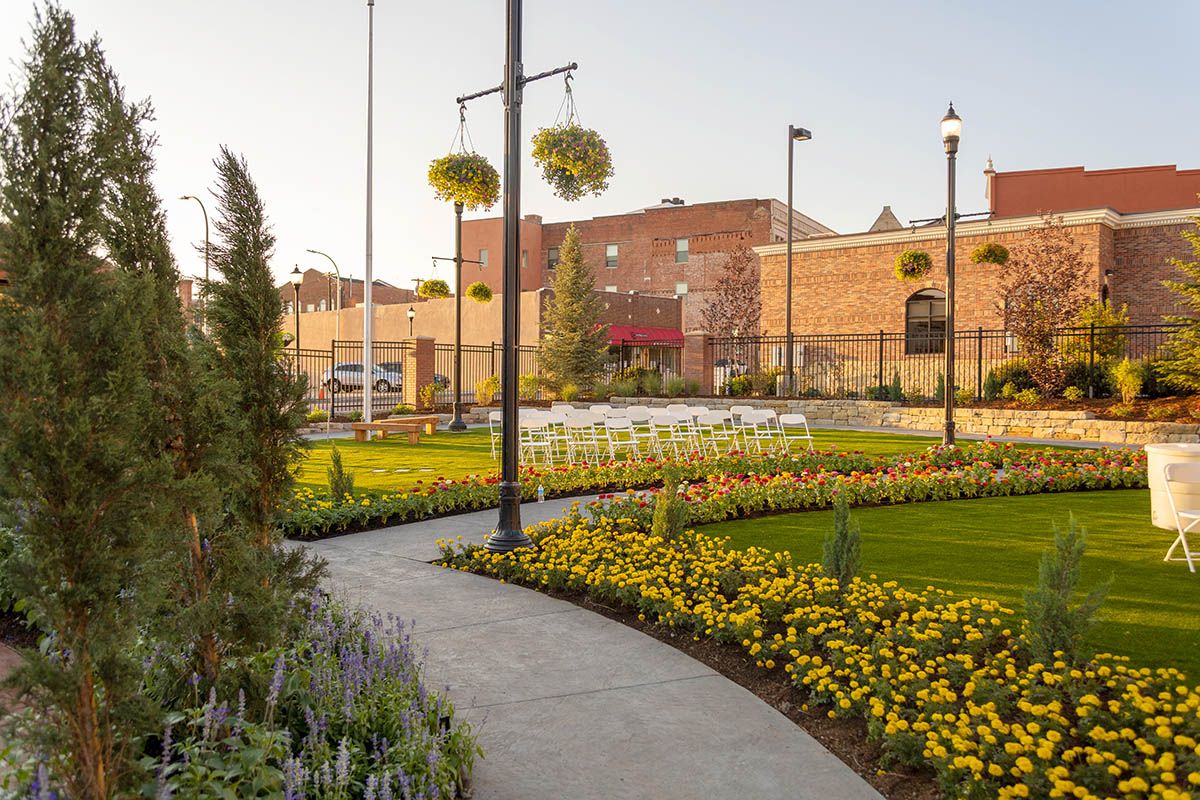 Landscaped garden path with yellow flowers, tall lamps, and historic brick buildings in the background