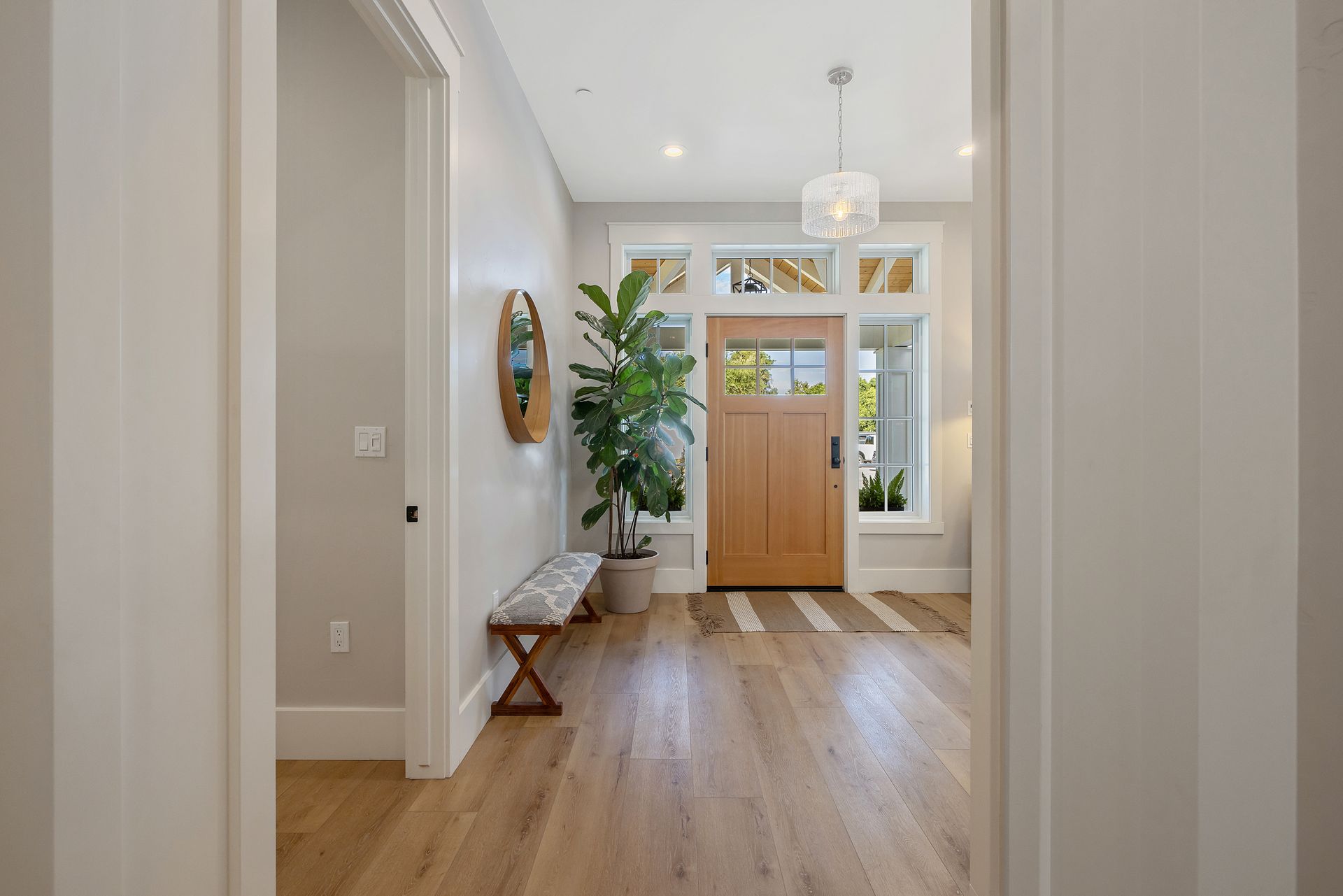 Bright entryway with wood floors, bench, potted plant, and double front doors with sidelights.
