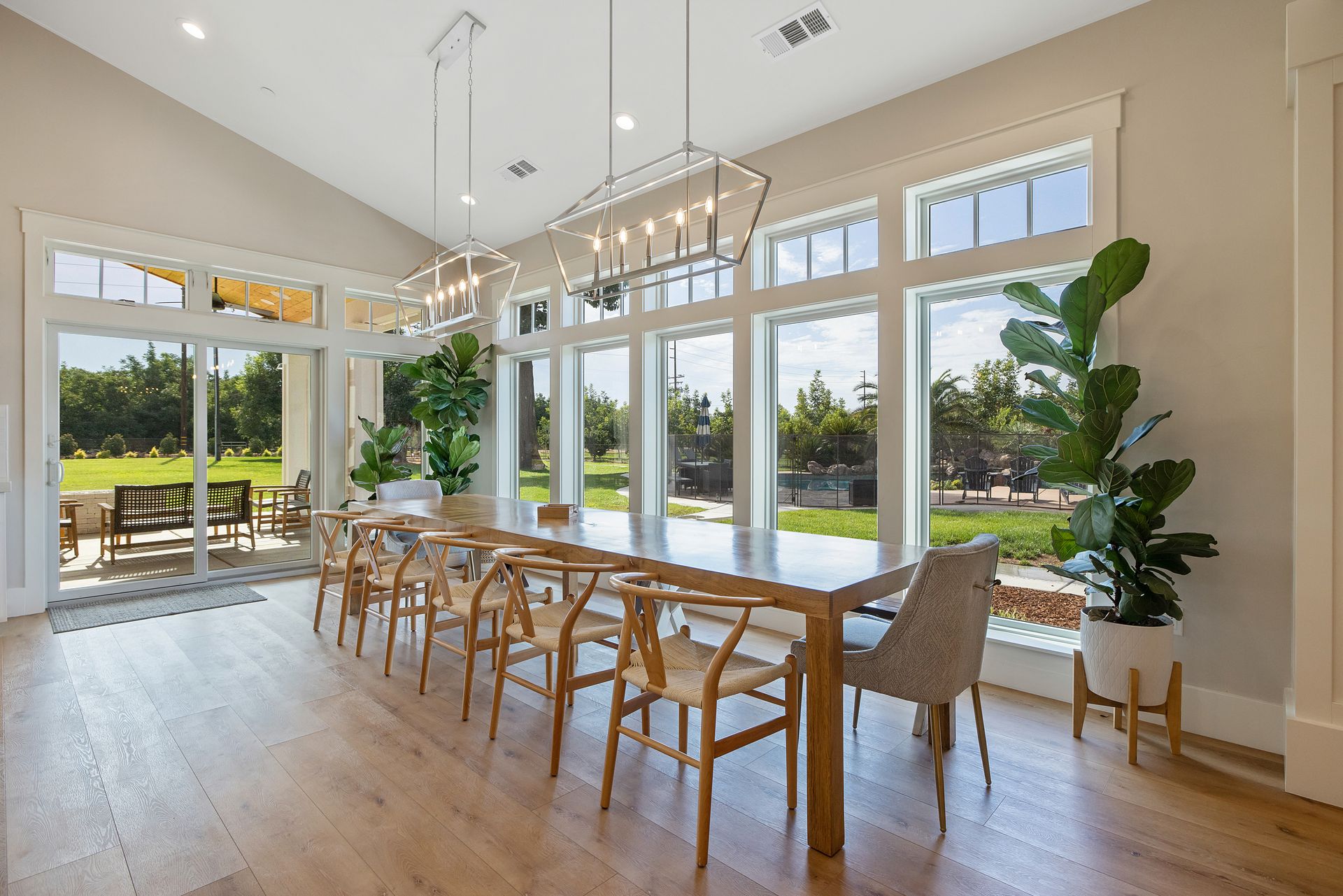 Bright modern dining room with large windows, long wooden table, and light wood chairs overlooking a pool.