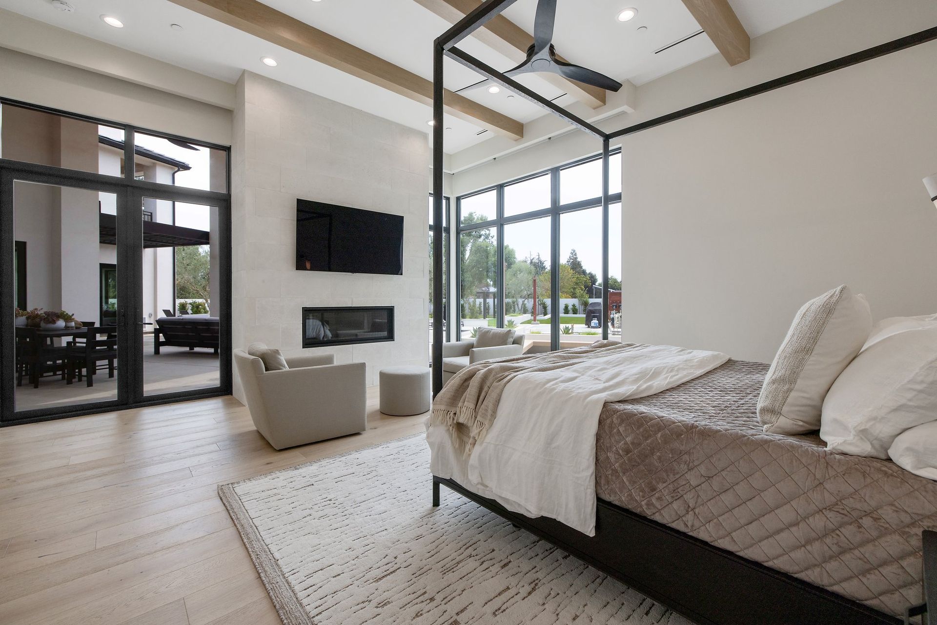 Modern bedroom with a large bed, wall-mounted TV, lounge chair, and floor-to-ceiling windows