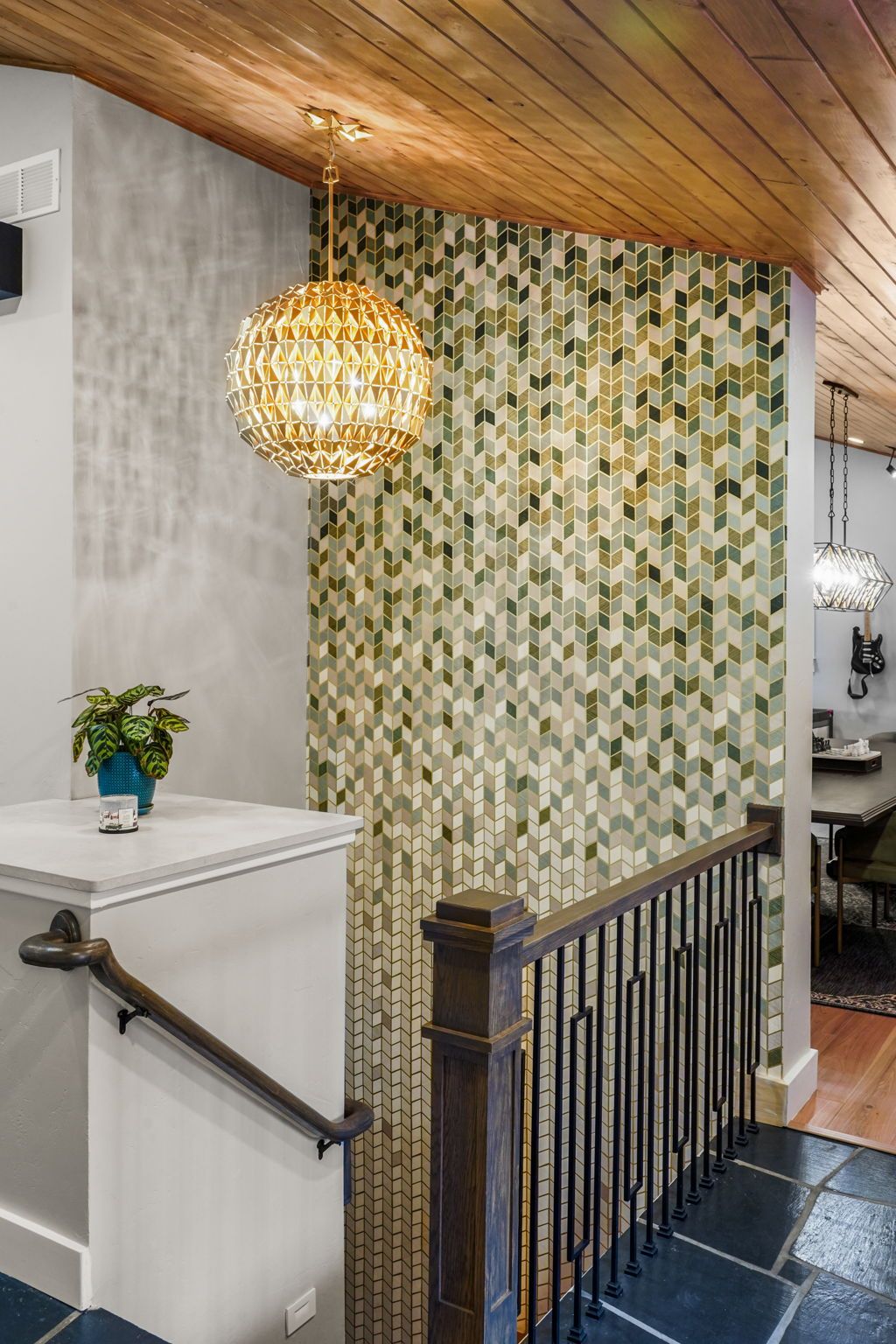 Hallway with green mosaic wall, wooden ceiling, pendant lights, and stair railing