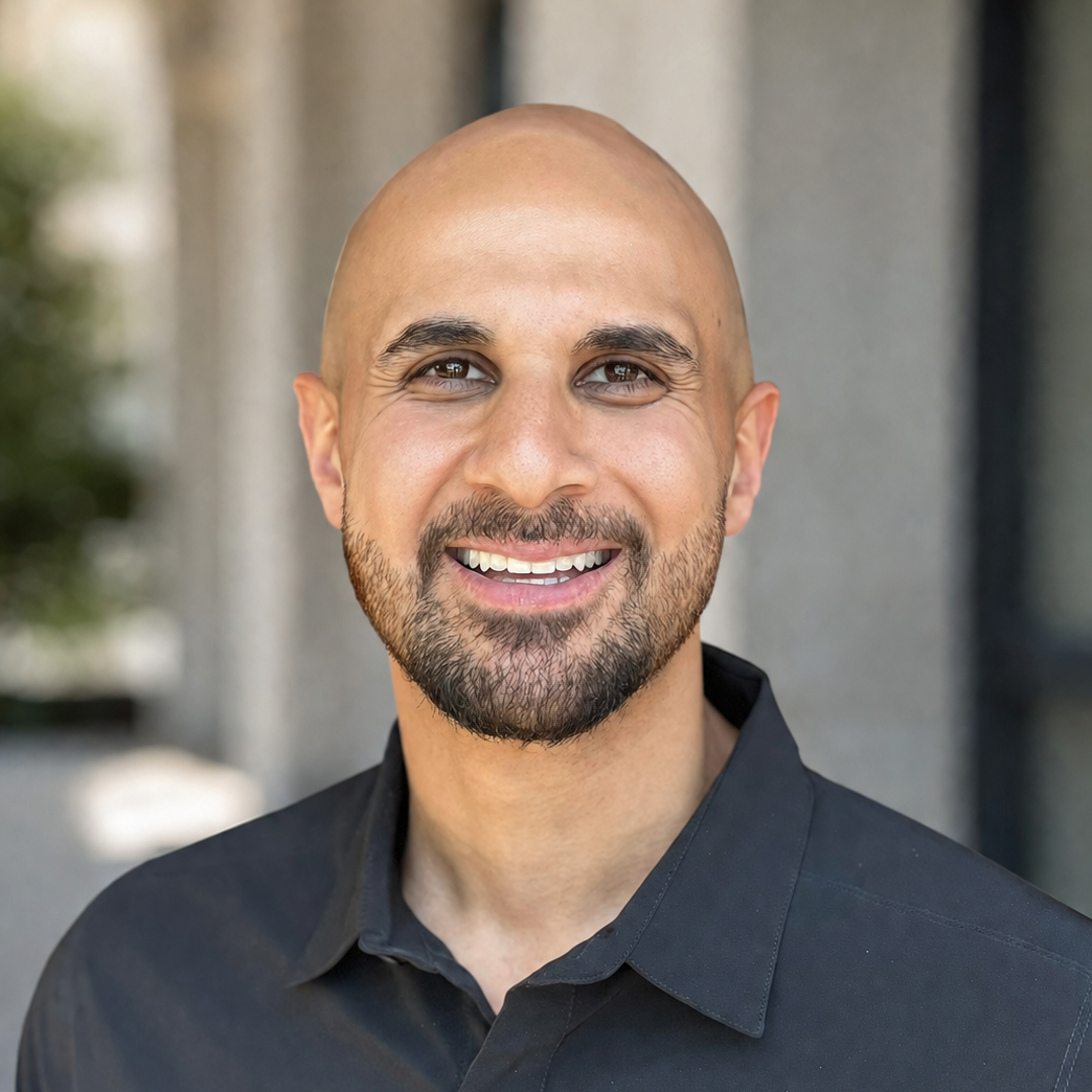 Smiling bald man with a short beard in a black shirt standing outdoors against a blurred background