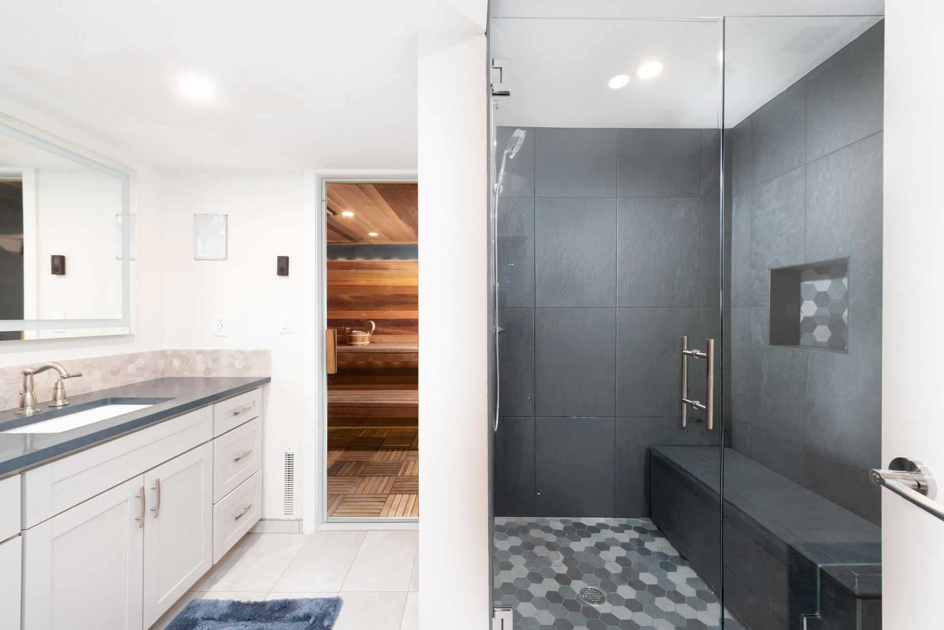 Bright bathroom with vanity on left and a tiled walk-in shower on right with a bench and glass door.