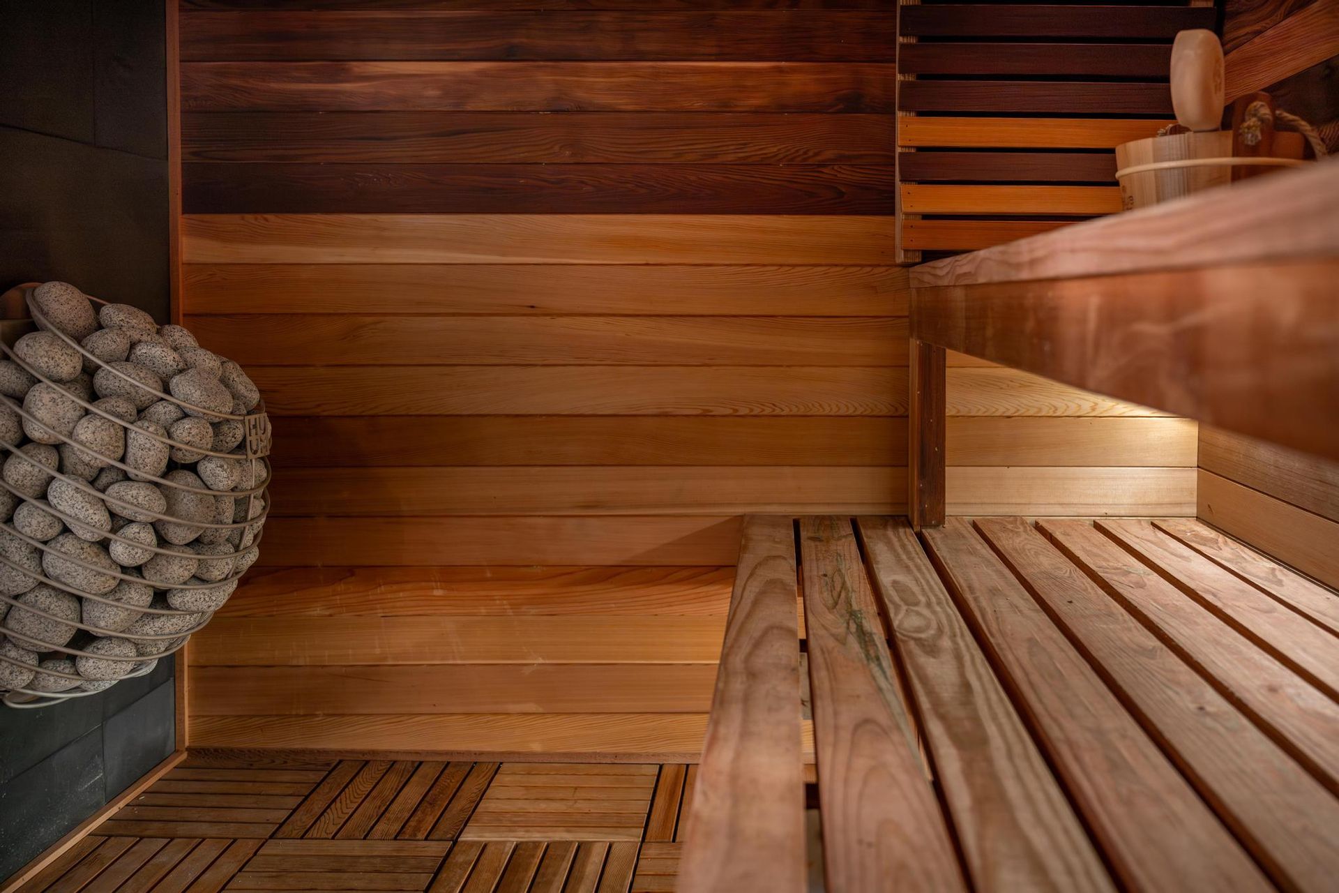 Wood-paneled sauna interior with wooden benches and a stone heater on the left