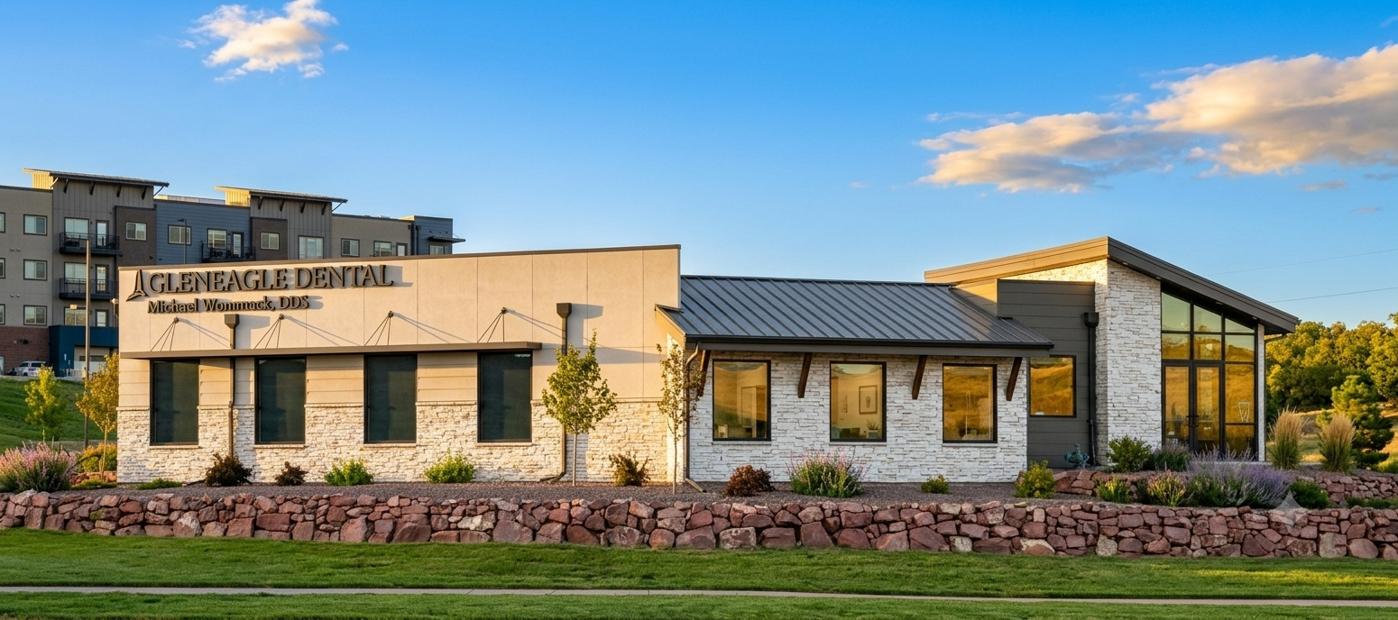 Single-story stone and brick building with a dark roof and landscaped flower bed at sunset