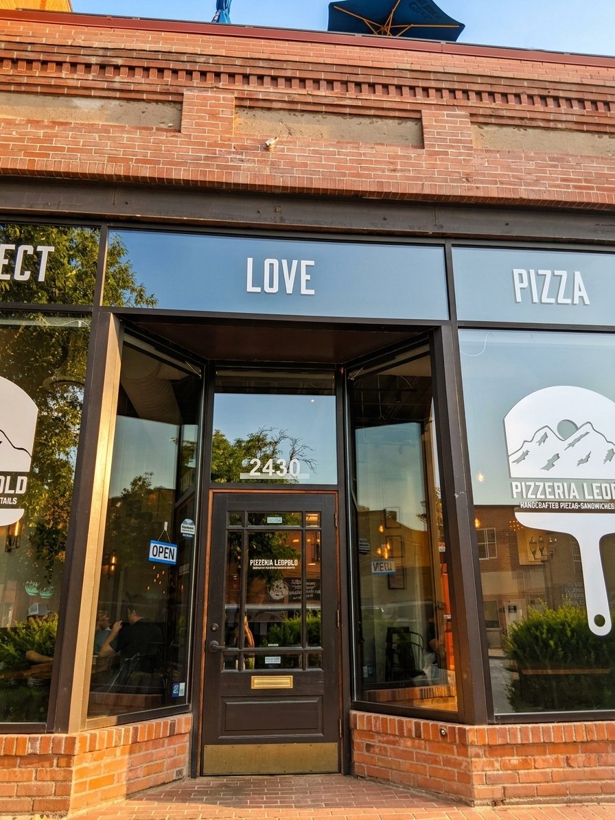 Brick storefront with black awning reading “LOVE” and “PIZZA” above a glass entrance.